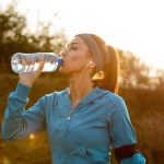 Young athletic woman drinking water with her eyes closed while having water break during morning run in nature.