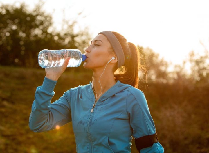Young athletic woman drinking water with her eyes closed while having water break during morning run in nature.